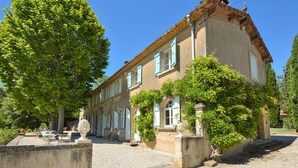Un bâtiment traditionnel avec une façade en pierre, de nombreuses fenêtres et une cour recouverte de gravier.