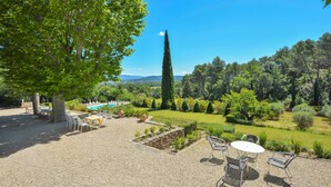 Un espace patio avec des sièges d’extérieur et une piscine, entouré d’une végétation luxuriante et offrant une vue sur la campagne.