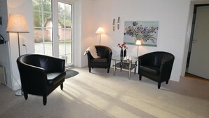 Una sala de estar moderna con dos sillones de cuero negro, una mesa de centro de cristal con velas y un cuadro en la pared.