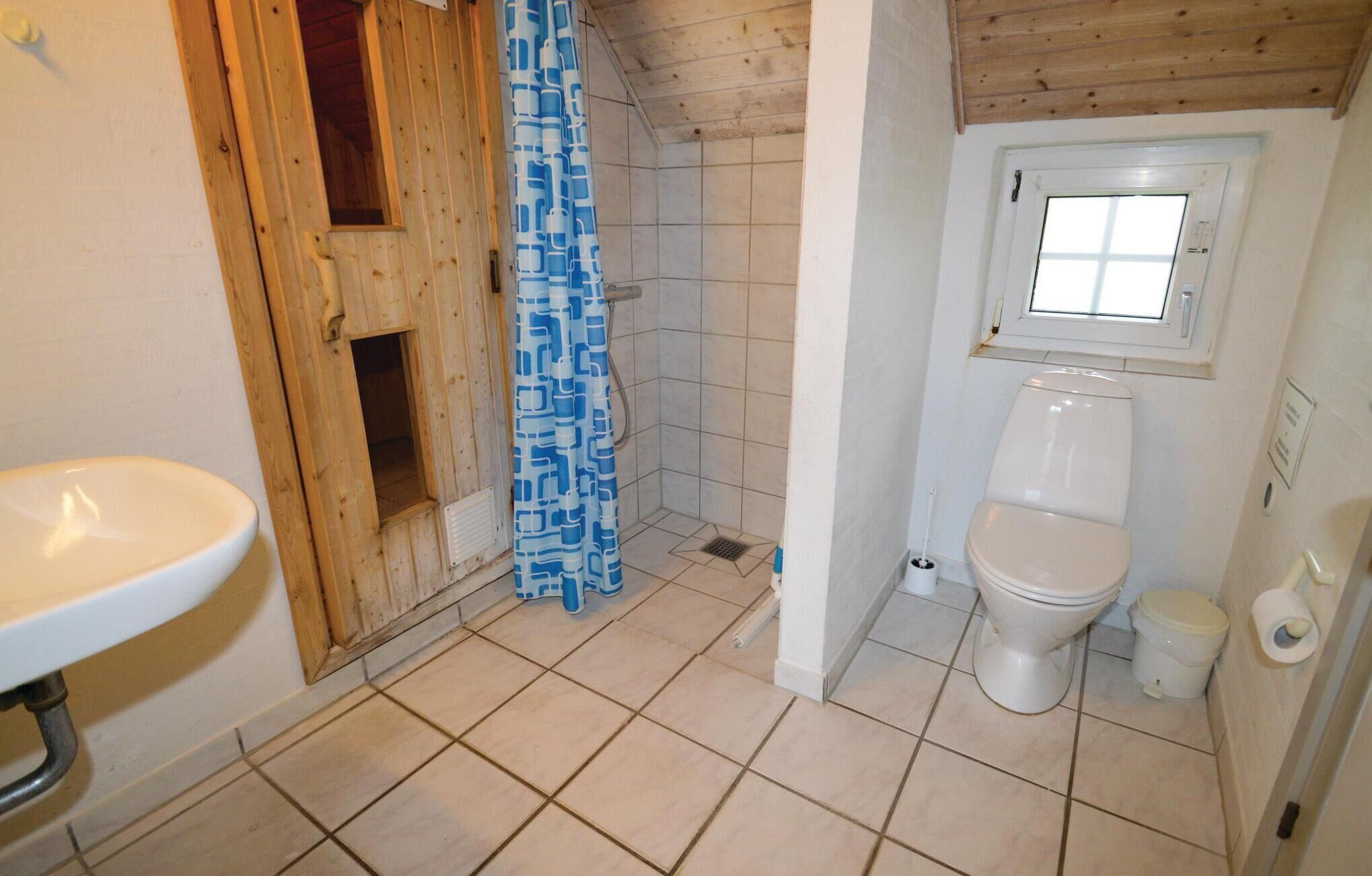 A bathroom with a wooden door, a shower with a blue patterned curtain, a white sink, and a toilet.