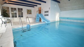 Una piscina interior con un tobogán azul, un área de descanso con sillas y vistas al área de la cocina.