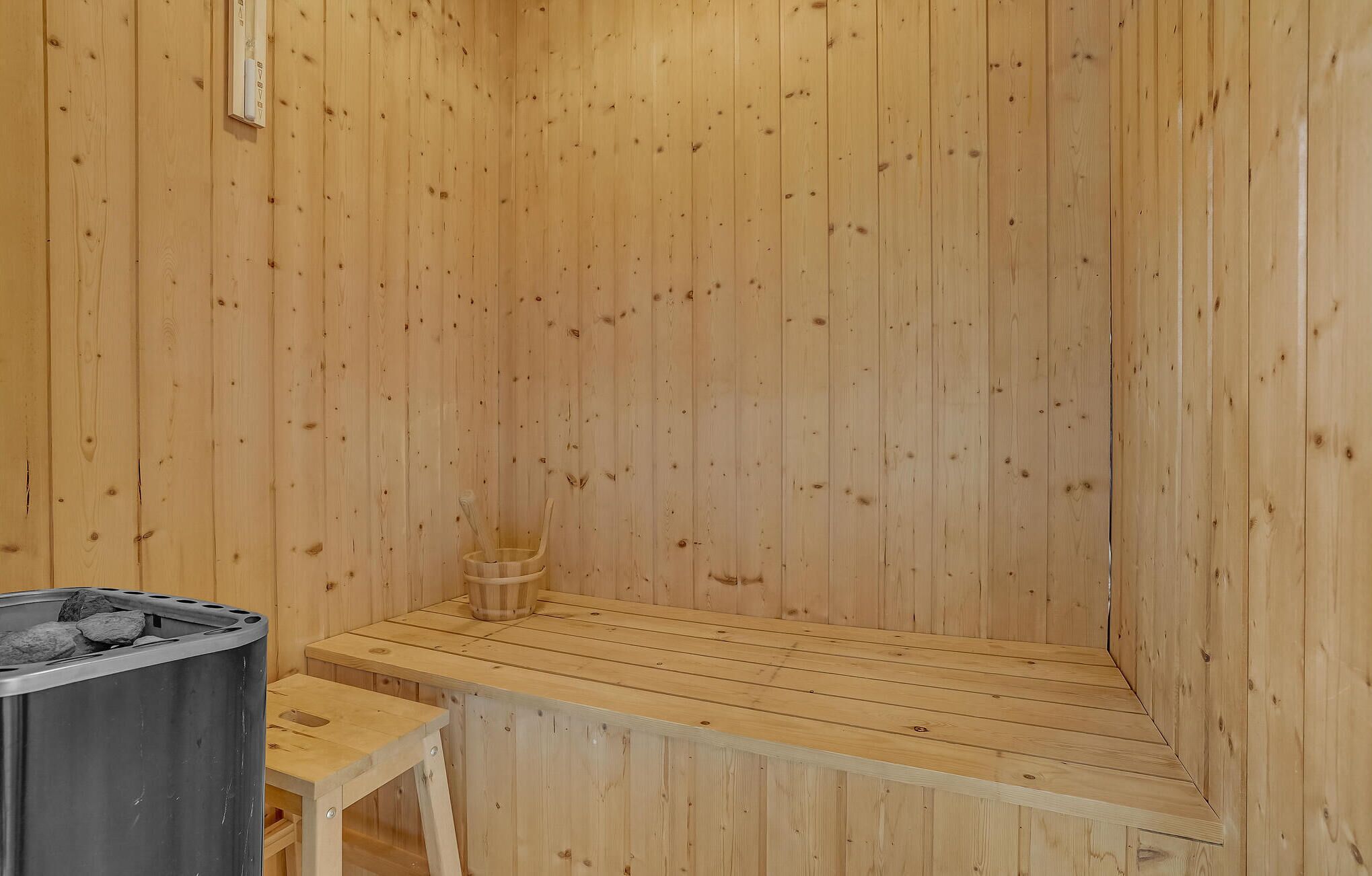 A wooden sauna with a bench, a small table, and a trash bin.