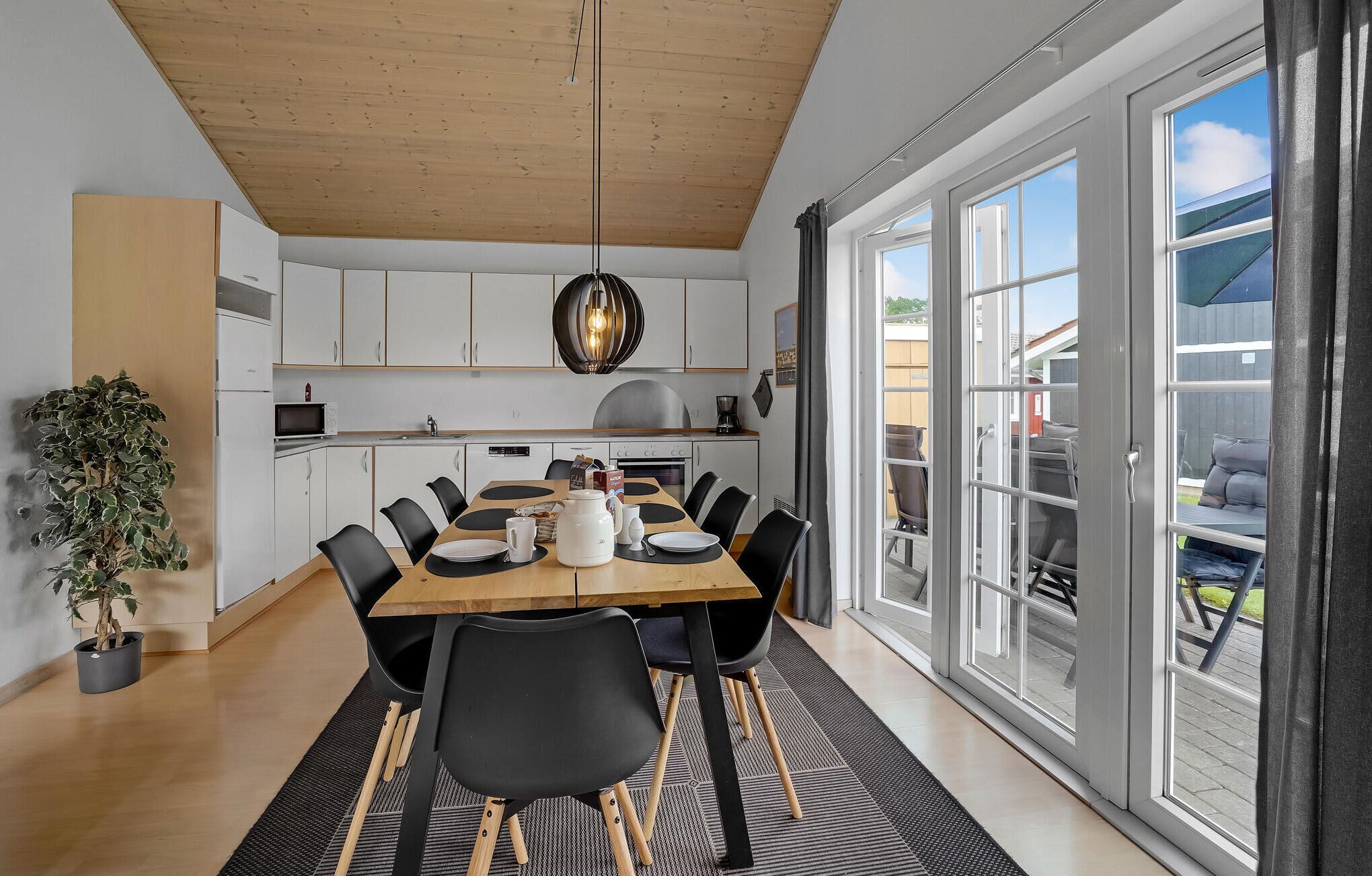 Une cuisine moderne avec des meubles blancs, un plafond en bois et un coin repas comprenant une grande table et des chaises.