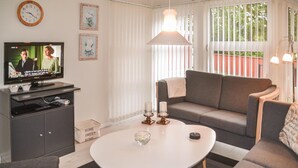 A living room with a grey sofa, a white coffee table, a TV on a stand, and a large window with blinds. - 3 bedroom gorgeous home in Oksbøl (Oksbøl)