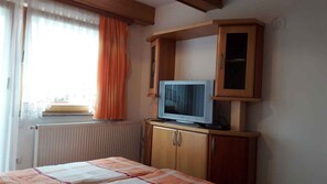 Ein Zimmer mit einem Bett, einem Fernseher auf einem Holzschrank und einem Fenster mit Vorhängen.