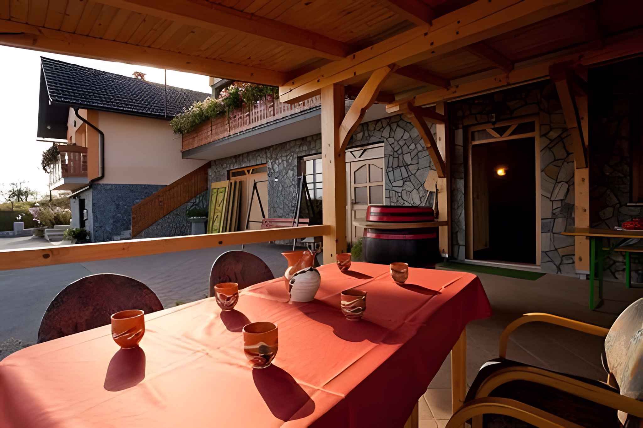 Un área de comedor al aire libre con mantel rojo, sillas de madera y un muro de piedra de fondo.