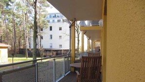 Uma varanda com cadeira e mesa de madeira, com vista para um edifício e árvores.