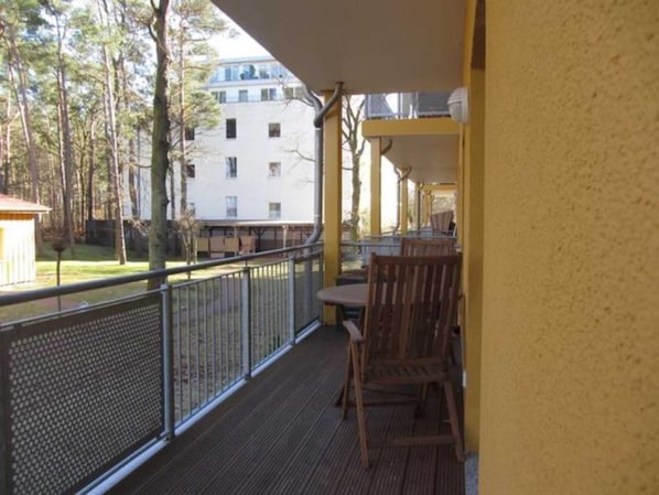 A balcony with a wooden chair and a table, overlooking a building and trees.