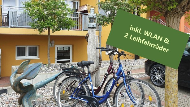 Uma bicicleta estacionada ao lado de um edifício com uma placa que diz 'inkl. WLAN & 2 Leihfahrräder'.