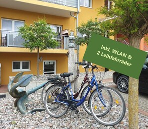 Uma bicicleta estacionada ao lado de um edifício com uma placa que diz 'inkl. WLAN & 2 Leihfahrräder'.