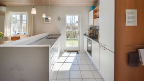A modern kitchen with a central island, white cabinetry, and a view through a glass door to the outdoors.