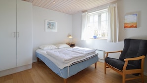 A bedroom with a bed, a chair, a window, and a painting on the wall.