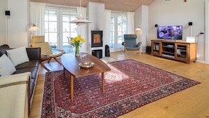 A living room with a wooden ceiling, a fireplace, a TV, and a large rug.