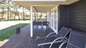 A covered outdoor area with a wooden deck, a table with chairs, and a grill.