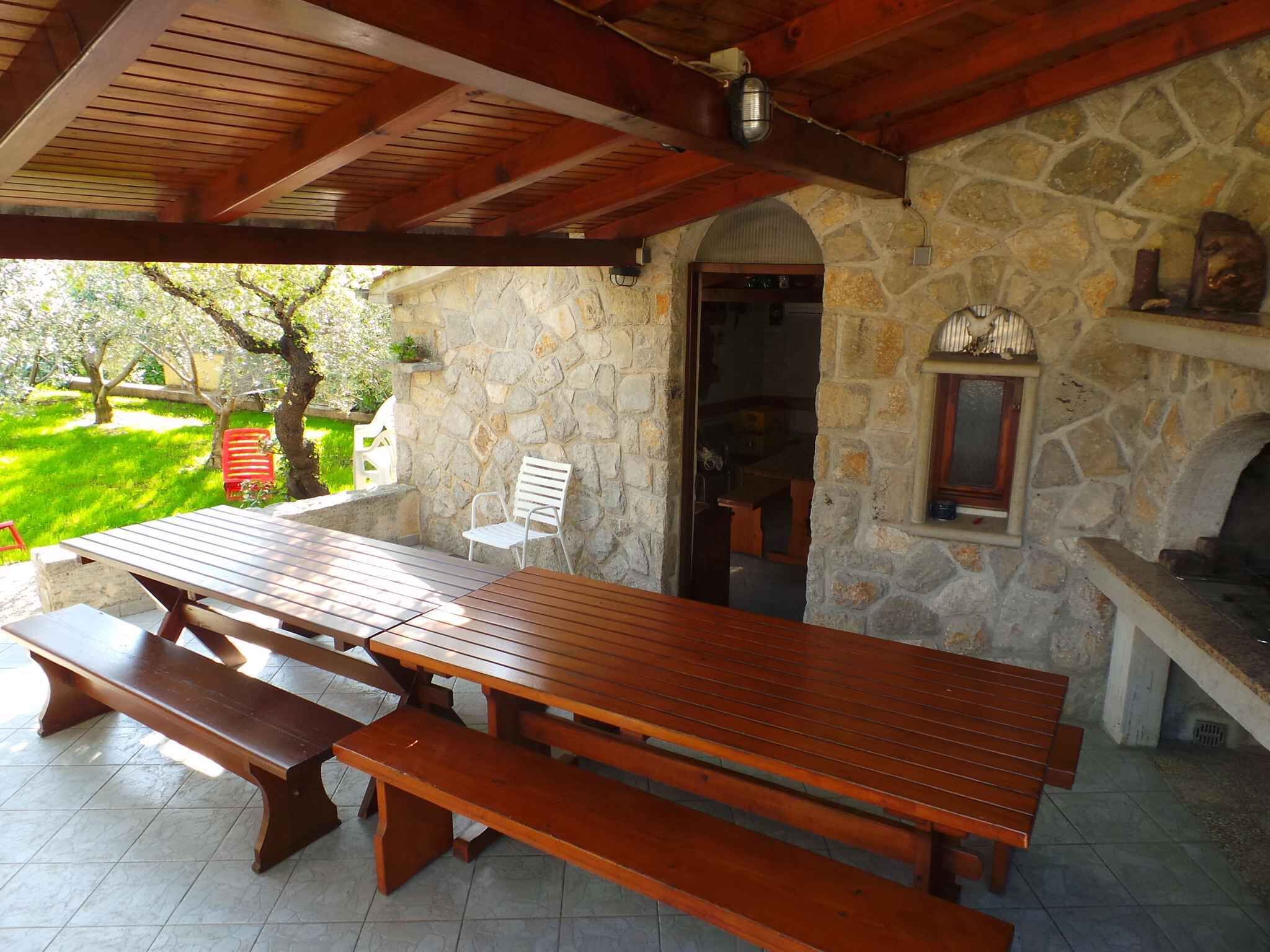 An outdoor patio with a stone wall, wooden benches, and a stone fireplace.