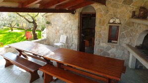 An outdoor patio with a stone wall, wooden benches, and a stone fireplace.