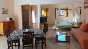 A room with a dining table, chairs, a sofa, a TV, and a bed with a canopy.