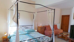 A four-poster bed with a canopy, a wooden nightstand with a lamp, a sofa, and a television on a wooden stand.
