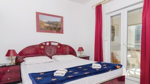 A hotel room with a bed, two bedside tables, a nightstand, a red curtain, a glass door, and a framed picture on the wall. - Lovely apartment in Zuljana with house sea view (Zuljana)