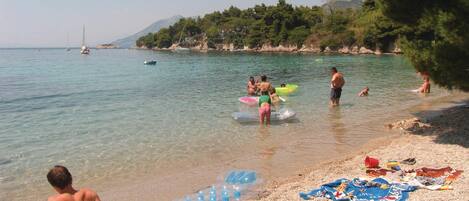 Una playa con agua cristalina, piedras y algunas personas.