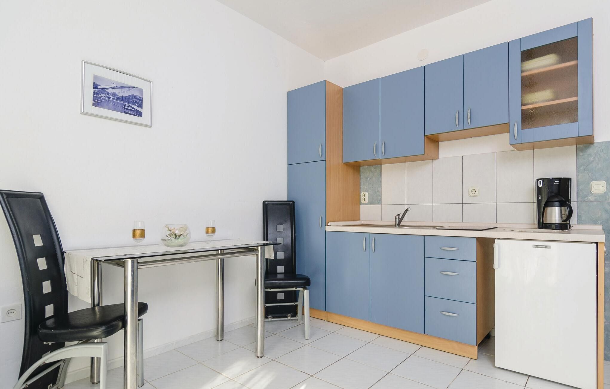 A compact kitchen with blue cabinets, a white countertop, a coffee maker, and a small refrigerator.