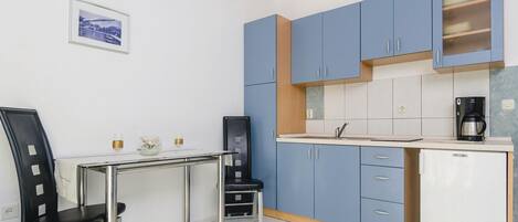 A compact kitchen with blue cabinets, a white countertop, a coffee maker, and a small refrigerator.