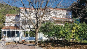 A building with a tiled roof, a tree in front, and a paved area with a bollard. - Lovely apartment in Zuljana with house sea view (Zuljana)