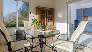 A sunlit patio with a round glass table, four chairs, a wooden cabinet, and a view of a blue kitchen through an open door. - Lovely apartment in Zuljana with house sea view (Zuljana)