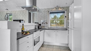 Una cocina moderna con armarios blancos, horno empotrado, ventana grande y pared decorada con ladrillos.