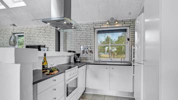 Une cuisine moderne avec des meubles blancs, un four encastré, une grande fenêtre et un mur décoratif en briques.
