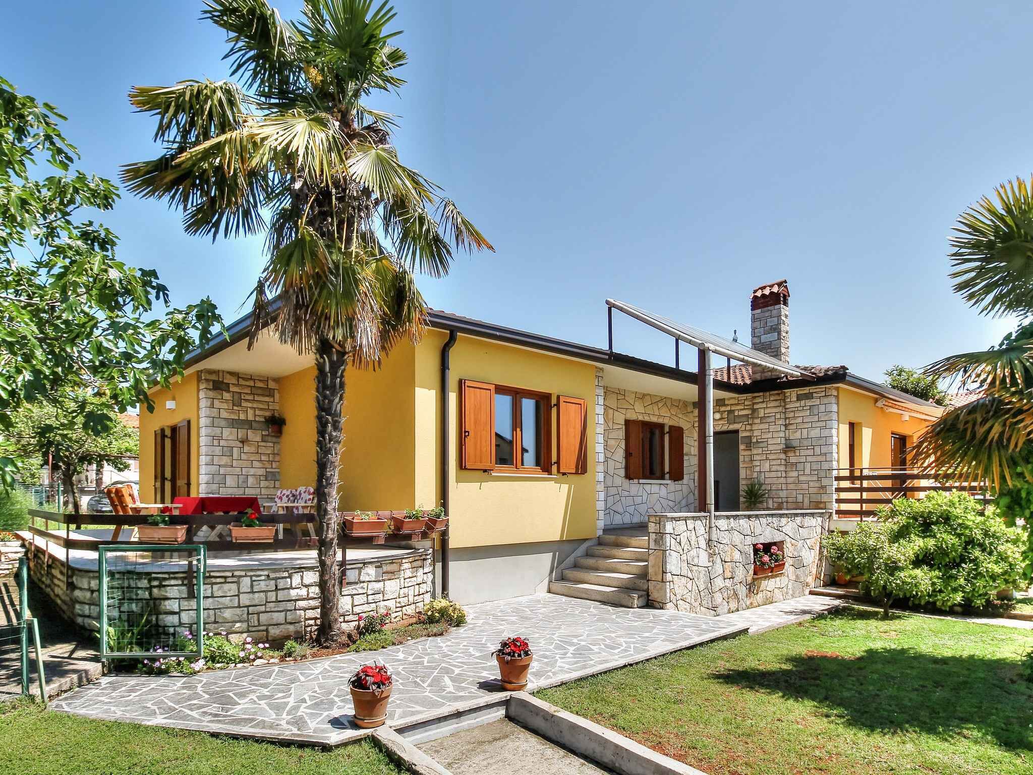 Uma casa de dois andares com fachada de pedra, exterior amarelo e uma pequena varanda com uma cadeira vermelha.
