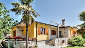 Una casa de dos pisos con fachada de piedra, exterior amarillo y un pequeño balcón con una silla roja.