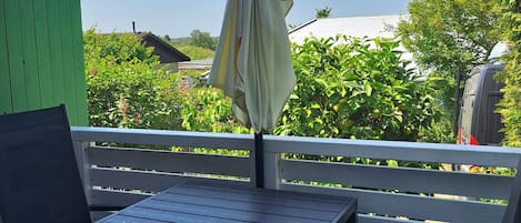 A wooden deck with a table and chairs, an umbrella, and a green fence.