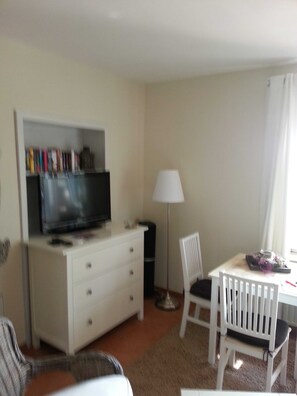 A room with a TV on a dresser, a lamp, a dining table with chairs, and a radiator.