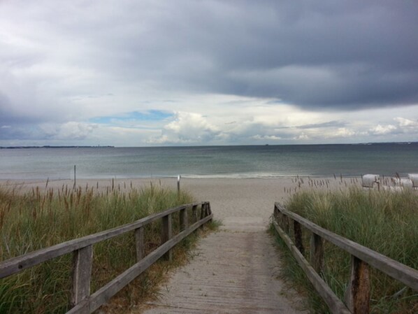 A wooden pathway leading to a beach with a cloudy sky.