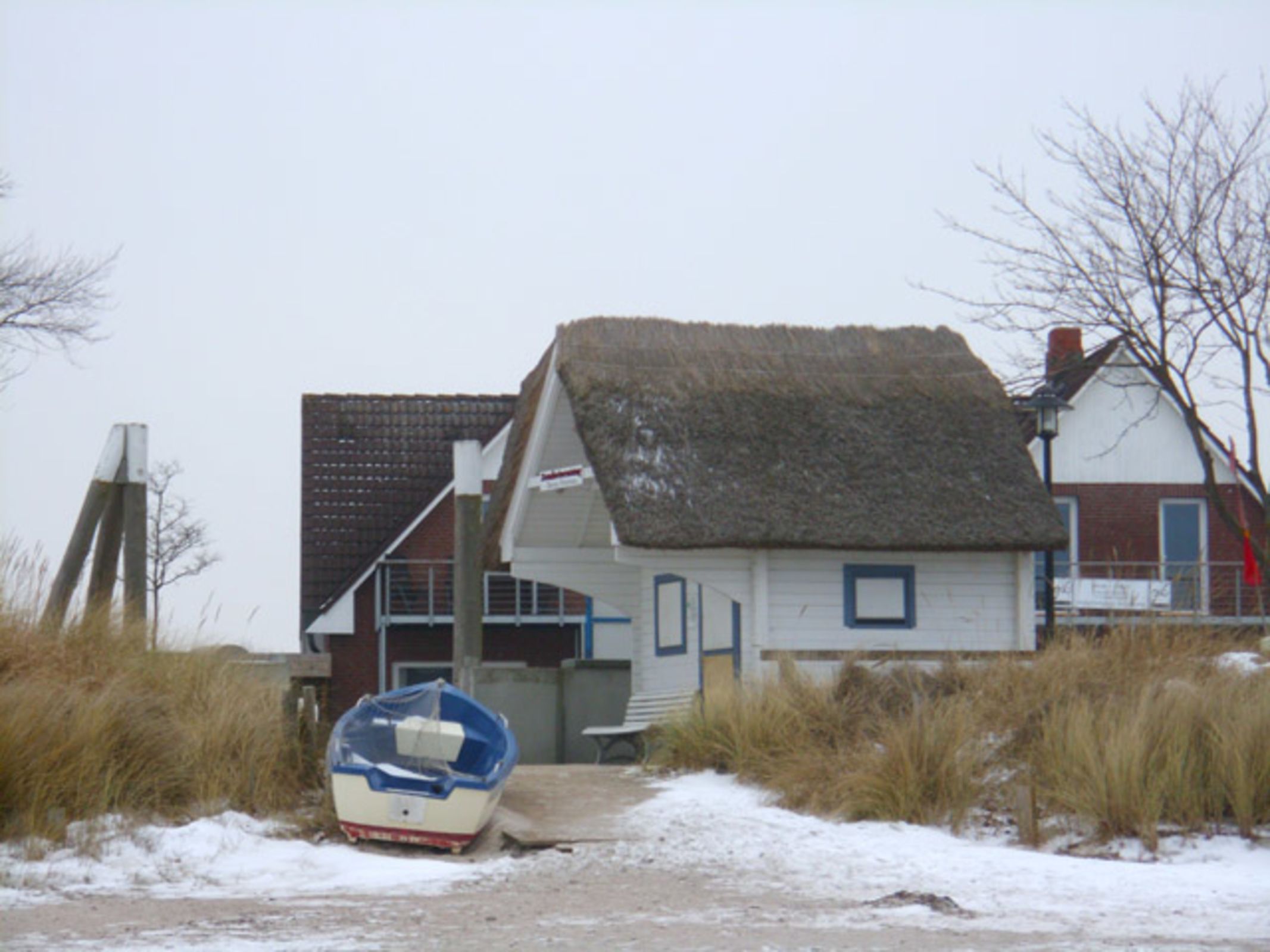 Une maison avec un toit de chaume, un bateau et un sentier sablonneux qui y mène.