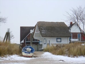 Une maison avec un toit de chaume, un bateau et un sentier sablonneux qui y mène.