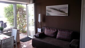 Ett vardagsrum med en soffa, ett bord och en stol. Det finns ett fönster med utsikt över träd och en bil som står parkerad utanför.