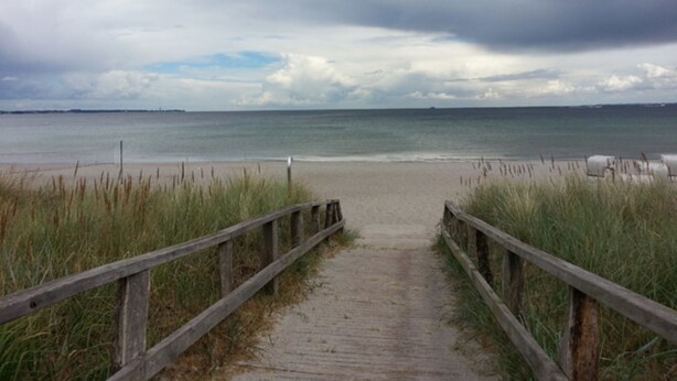 En träpromenad som leder till en strand med en molnig himmel.