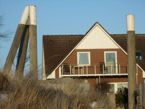 A two-story building with a brick facade, a white roof, and a balcony with railings.