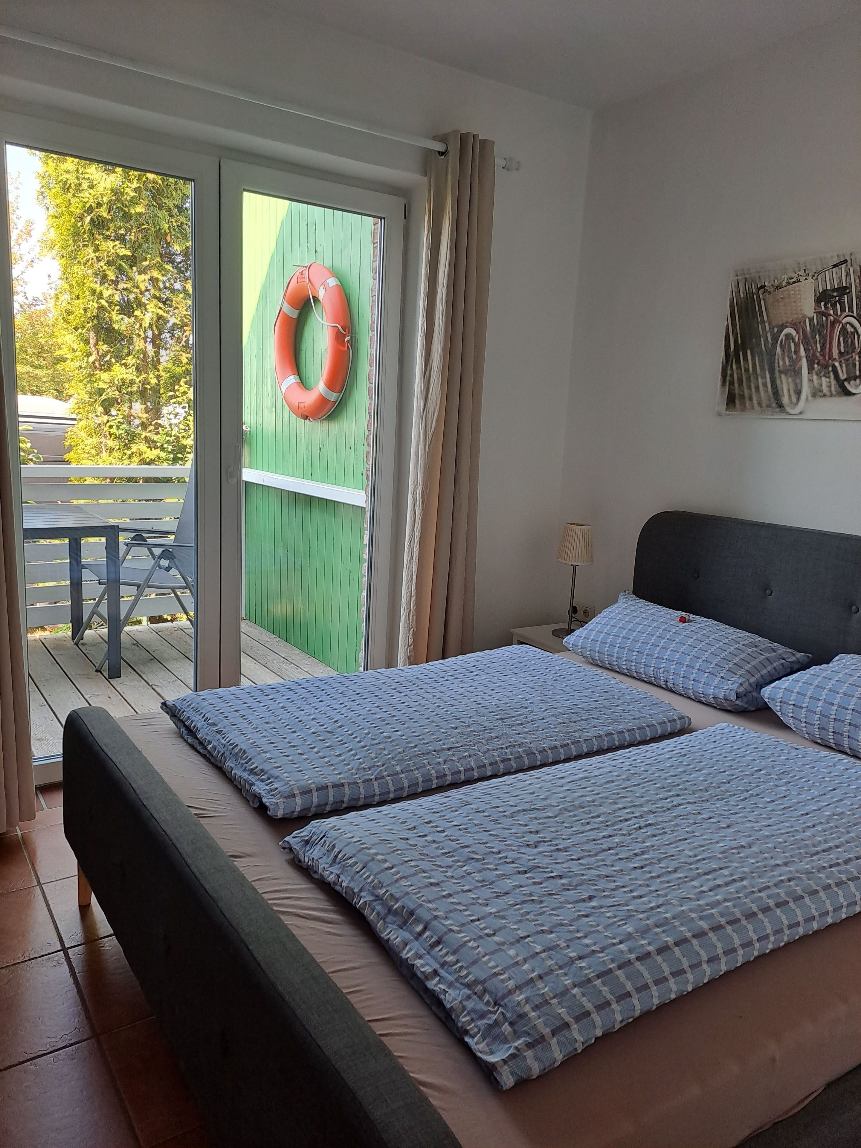 Een slaapkamer met een bed, een kussen, een nachtkastje, een lamp, een reddingsboei en uitzicht op de omgeving.