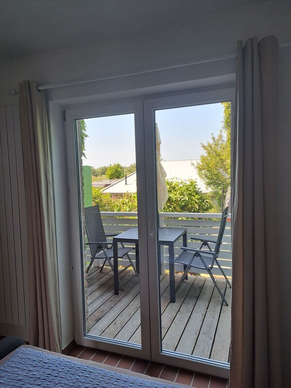 Quarto com porta de vidro deslizante que dá para um pátio externo com mesa e cadeiras.