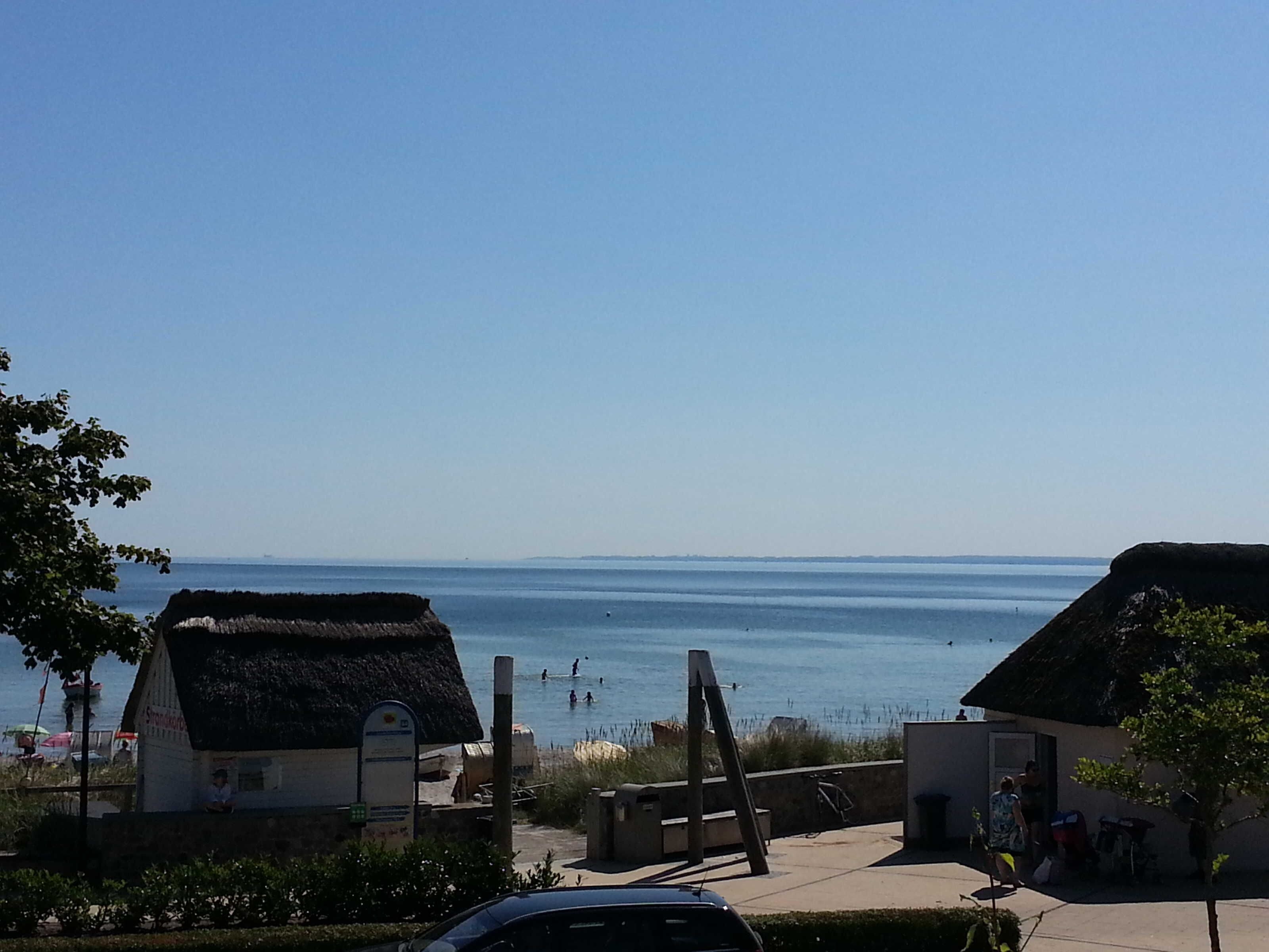 Une vue sur la côte, avec des bâtiments aux toits de chaume, un ciel dégagé et une mer calme.