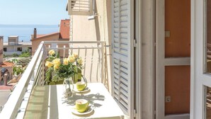 Un balcon avec une table dressée pour deux personnes, un vase rempli de fleurs jaunes et une vue sur la mer.