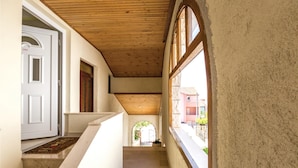 Un couloir avec un plafond en bois, une porte blanche et une vue sur l’extérieur.