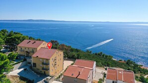 Complejo de edificios costeros con varios balcones, un patio empedrado y vista al mar.