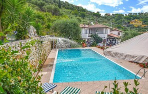 Une piscine rectangulaire, avec un mur en pierre d’un côté et une zone abritée de l’autre.