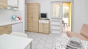 A modern, well-lit room with a white table, a sofa, a TV, and a wardrobe. - Studio with air conditioning and terrace (Baška)