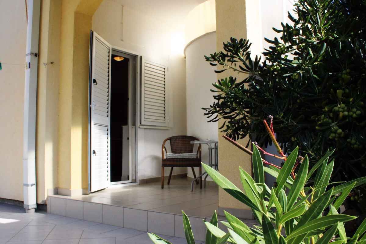 Ein Außenbereich mit einer zur Wohnung führenden Tür, einem Sessel und einem Blumentopf.