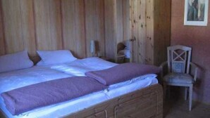 Una cama de madera con colchón y almohadas, un armario de madera y una silla en una habitación con paredes de madera.